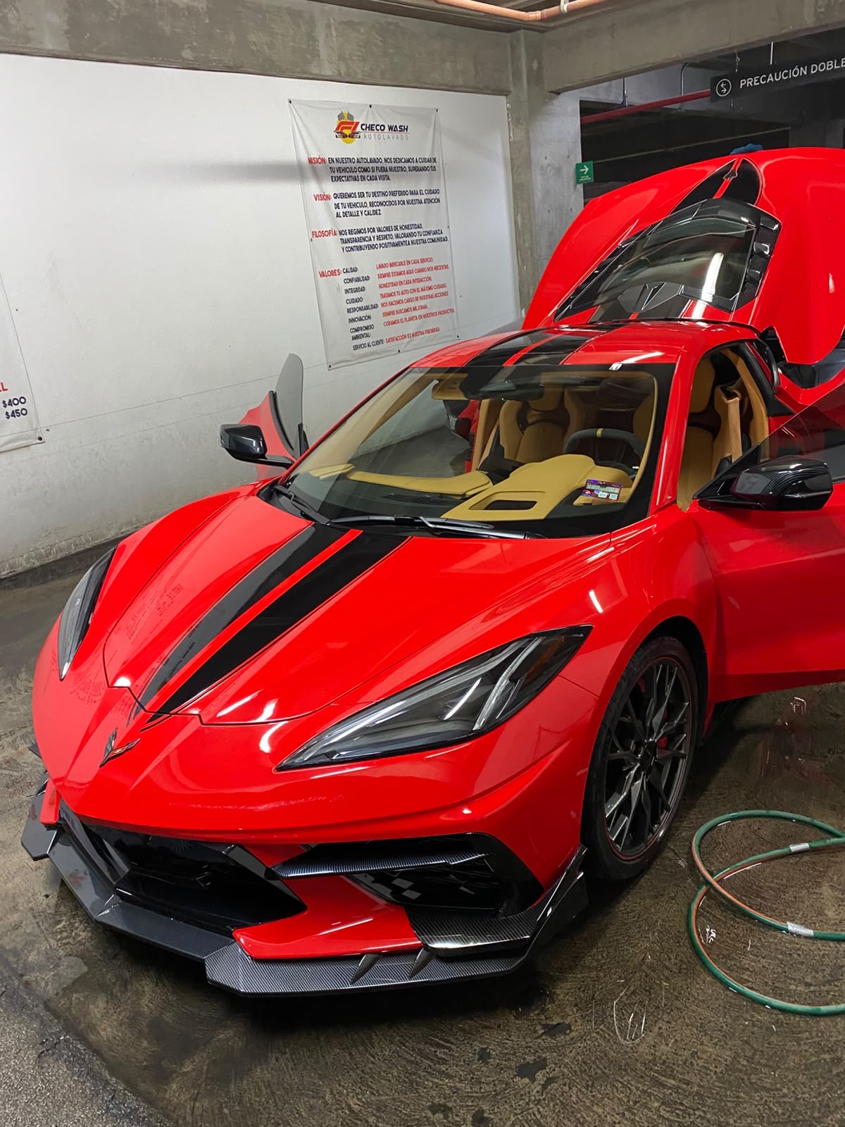 Chevrolet Corvette rojo con franjas negras y puertas abiertas, recién lavado dentro de la nave de Checo Wash